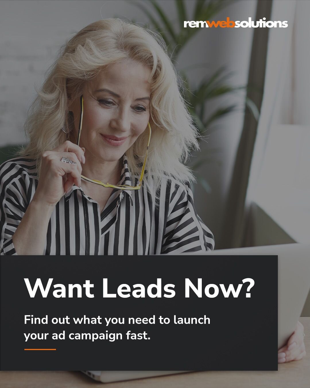 Woman smiling and holding her glasses while looking at laptop.