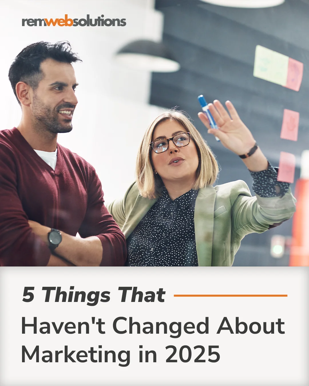 Man and woman standing pointing to sticky notes on glass wall